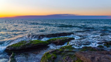 Gün batımında dalgalar kayalık sahile çarpıyor.