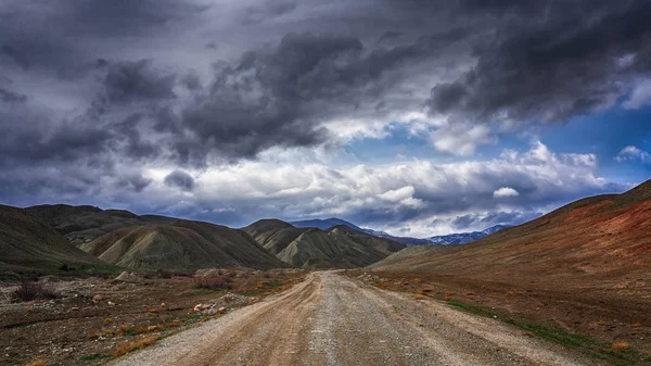 Estrada de terra para as montanhas em tempo tempestuoso — Fotografia de Stock