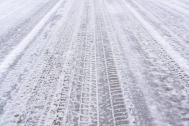 Karlı bir yolda araba izleri var.