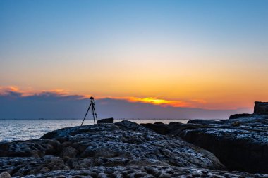 Bir tripodun üzerindeki kamera denizde renkli bir gündoğumu çeker.