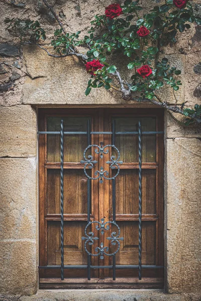 Facade of a mediterranean traditional house with a wooden latticed window and red climbing roses