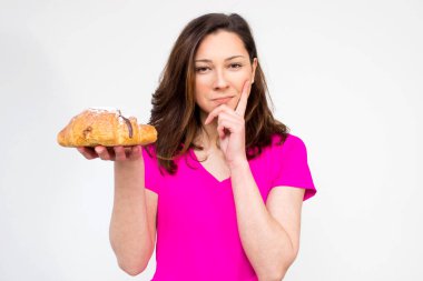 Pembe gömlekli uygun kadın kruvasan yemek istiyor, kruvasan kız genç kadınla kruvasan yemek için tereddüt. izole değil