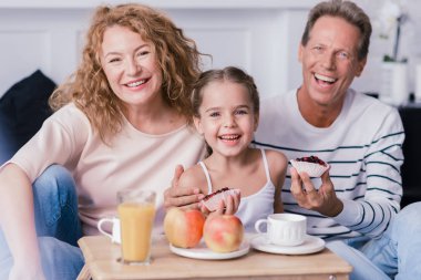 Smiling little girl holding berry cupcakes with her grandparents clipart