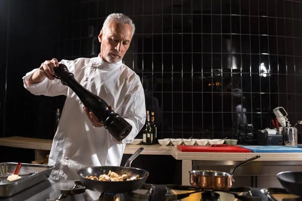 Resolved chef putting salt on fried mushrooms — Stock Photo, Image