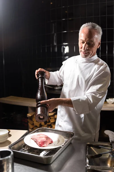 Bearded happy chef putting salt on the steak — Stock Photo, Image