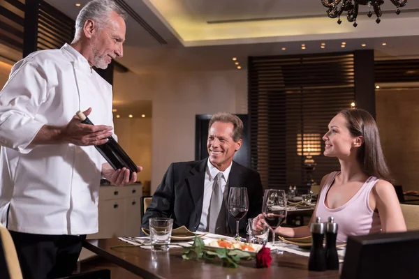 Cheerful chef advising a bottle of wine to the couple — Stock Photo, Image