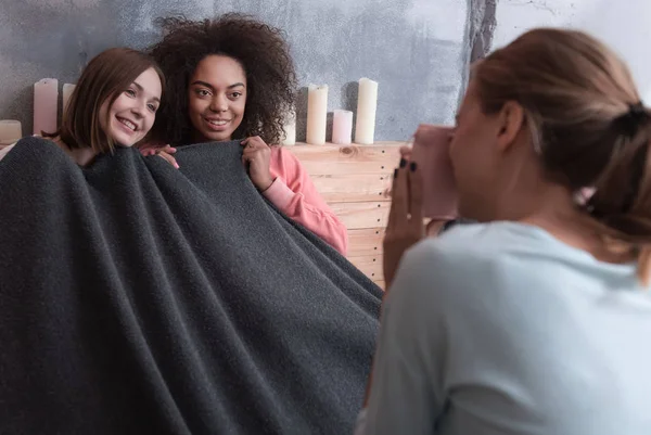 Приятные улыбающиеся девушки, покрытые одеялом дома — стоковое фото