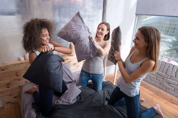 Riendo amigos de pie en la cama y teniendo pelea de almohadas —  Fotos de Stock