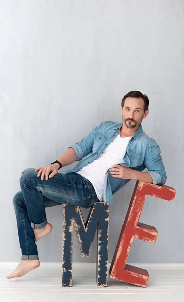 Nice positive man sitting on the huge wooden letters — Stock Photo, Image