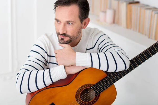Thoughtful attractive man leaning his elbows on the guitar — Stock Photo, Image