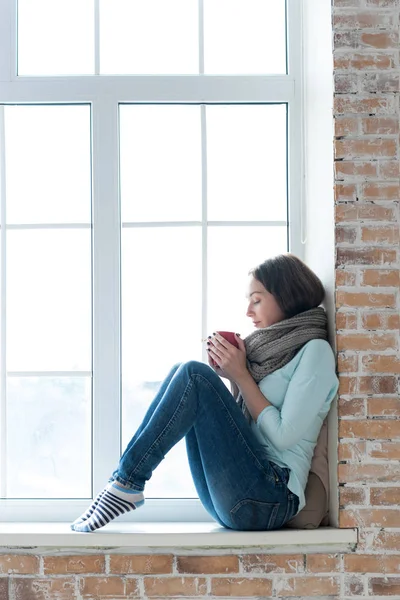 Attractive young woman sitting alone on a windowsill — Stock Photo, Image