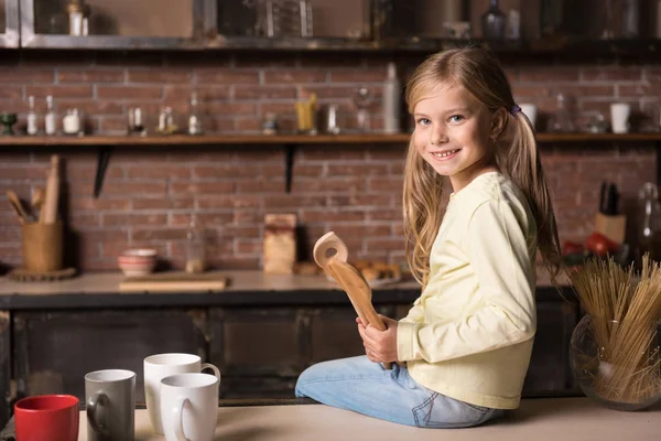 Uśmiechnięte dziewczyny, trzymając drewniane łyżki i siedzi na stole — Zdjęcie stockowe