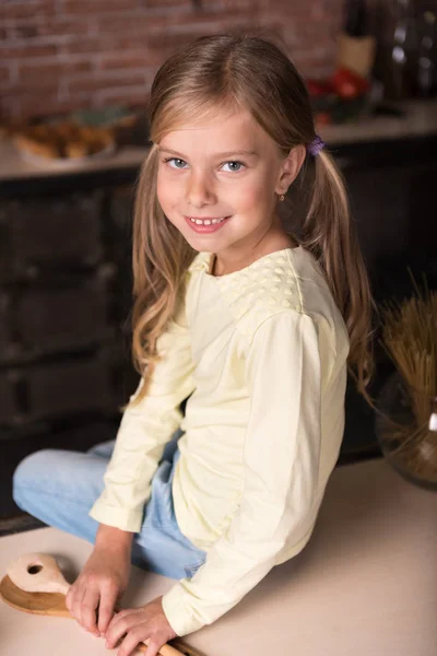 木製のスプーンを押しながら、テーブルの上に座って微笑んでいる女の子 — ストック写真