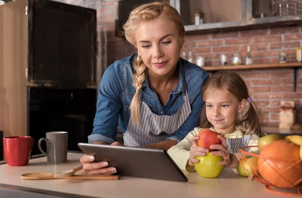 Söt flicka läsa recept med mamman i köket — Stockfoto