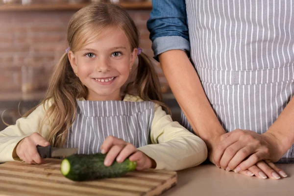 Fröhliches kleines Mädchen beim Gurkenschneiden in der Küche — Stockfoto