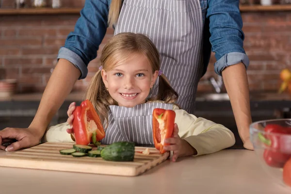 Divertida niña sosteniendo un pimiento cerca de su madre —  Fotos de Stock