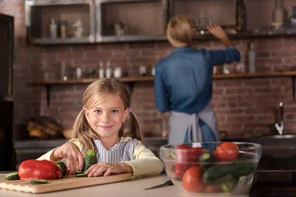 Lächelndes kleines Mädchen, das Gemüse in der Küche berührt — Stockfoto