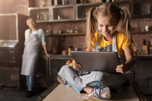 Glückliches kleines Mädchen beim Blick auf das Tablet in der Küche — Stockfoto