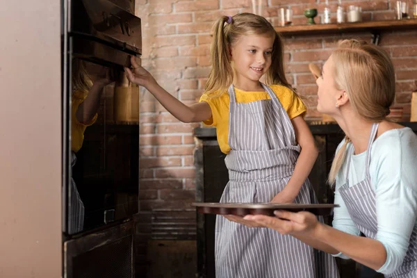 Chica involucrada poniendo con su madre pastelería en el horno —  Fotos de Stock