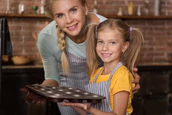 Leende flicka sätta med hennes mor bakverk i ugnen — Stockfoto