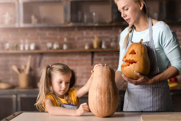 Concentrated girl decorating jack o lantern with her mother — Stock Photo, Image