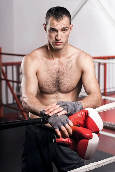 Hombre apoyado en la cuerda del anillo mientras sostiene guantes de boxeo — Foto de Stock