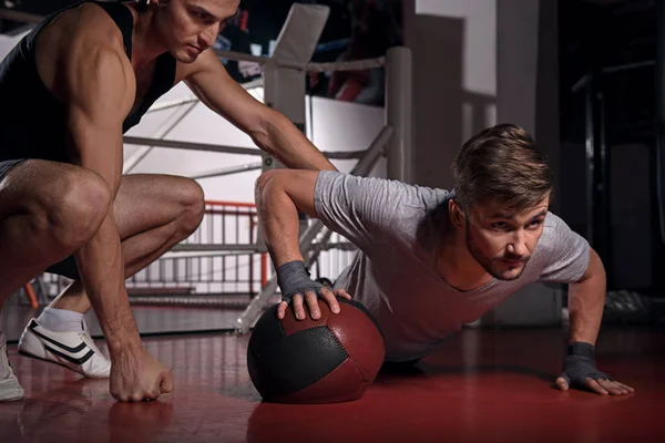 Mann macht Liegestütze mit Trainer mit Fitnessball — Stockfoto