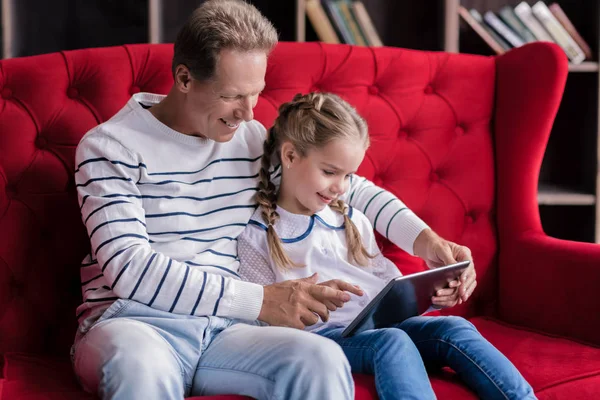 Hermosa chica descansando con su abuelo y sosteniendo la tableta —  Fotos de Stock