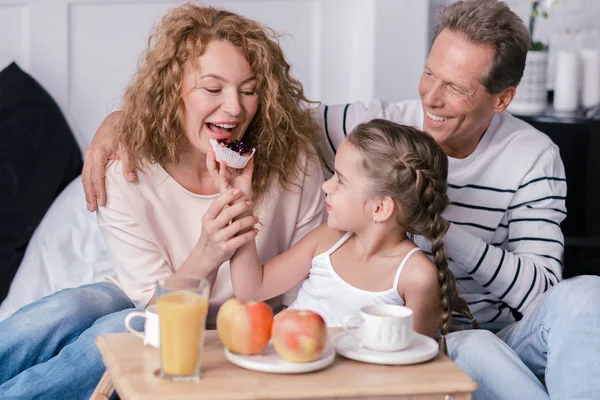 Amused girl eating berry cupcakes with her grandparents