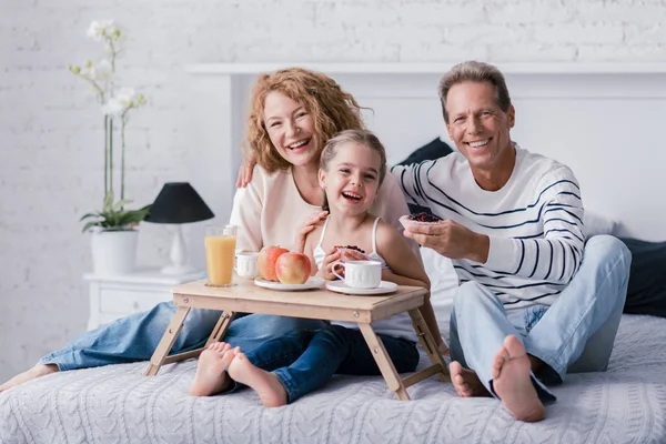 Happy girl sitting at the breakfast tray with her grandparents — Stock Photo, Image