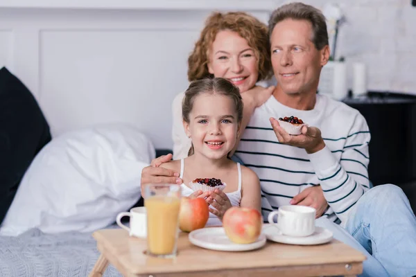 Iloinen pieni tyttö, jolla on marjakakkuja isovanhempiensa kanssa — kuvapankkivalokuva