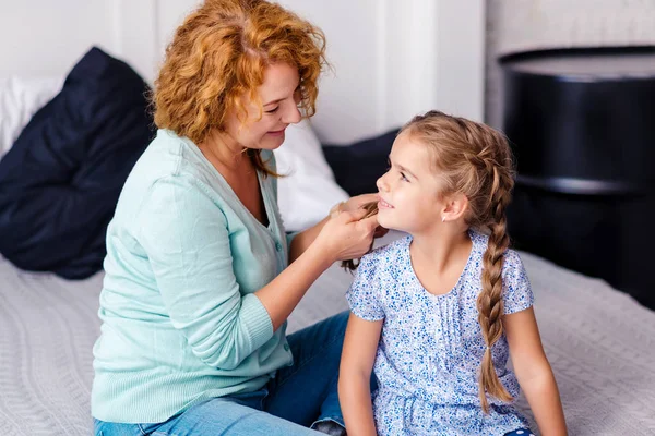 Smiling grandmother plaiting braids to her granddaughter — Stock Photo, Image