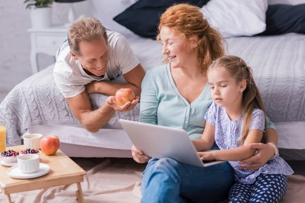 Flickan sitter framför den bärbara datorn med hennes morföräldrar — Stockfoto