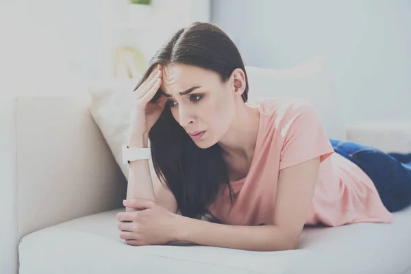 Jovem mulher bonita deitada no sofá e com enxaqueca . — Fotografia de Stock