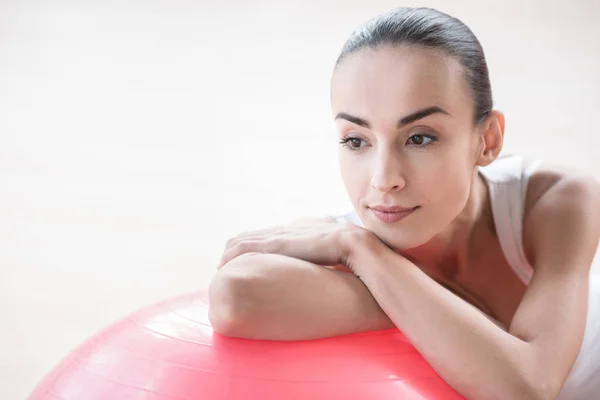 Sério mulher pensativa apoiando-se em uma bola de fitness rosa — Fotografia de Stock