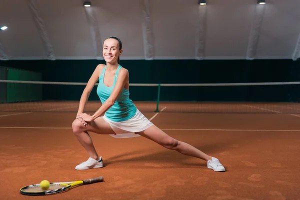 Mujer alegre haciendo ejercicios deportivos en pista de tenis cubierta — Foto de Stock