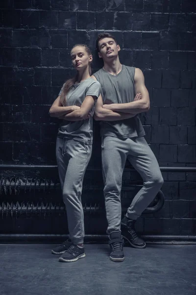 Bailarines concentrados de pie cerca de la pared negra con los brazos cruzados — Foto de Stock