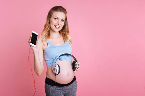 怀孕女运动员把耳机放在她的肚子上 — 图库照片