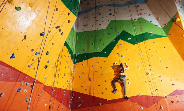 Mulher confiante subindo a parede laranja no ginásio — Fotografia de Stock