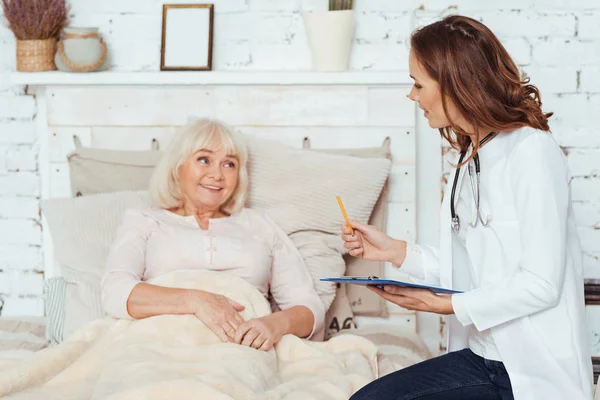 Professionale medico femminile positivo esaminare il suo paziente a casa — Foto Stock