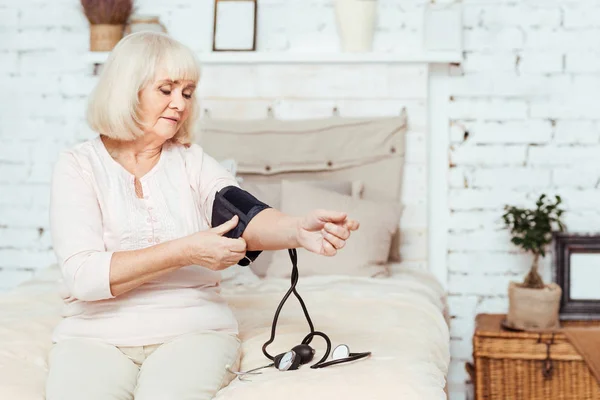 Mulher idosa sem alegria medindo a pressão arterial — Fotografia de Stock