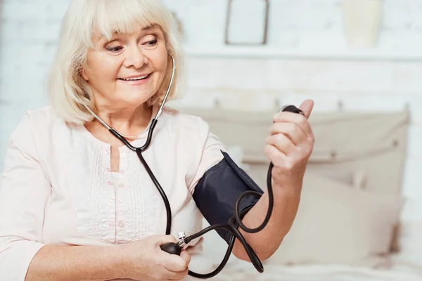 Mujer anciana sonriente midiendo la presión arterial — Foto de Stock