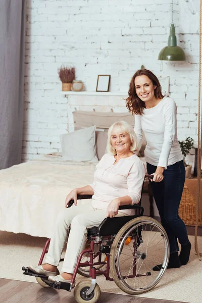 Joful mujer sosteniendo silla de ruedas con su abuela — Foto de Stock