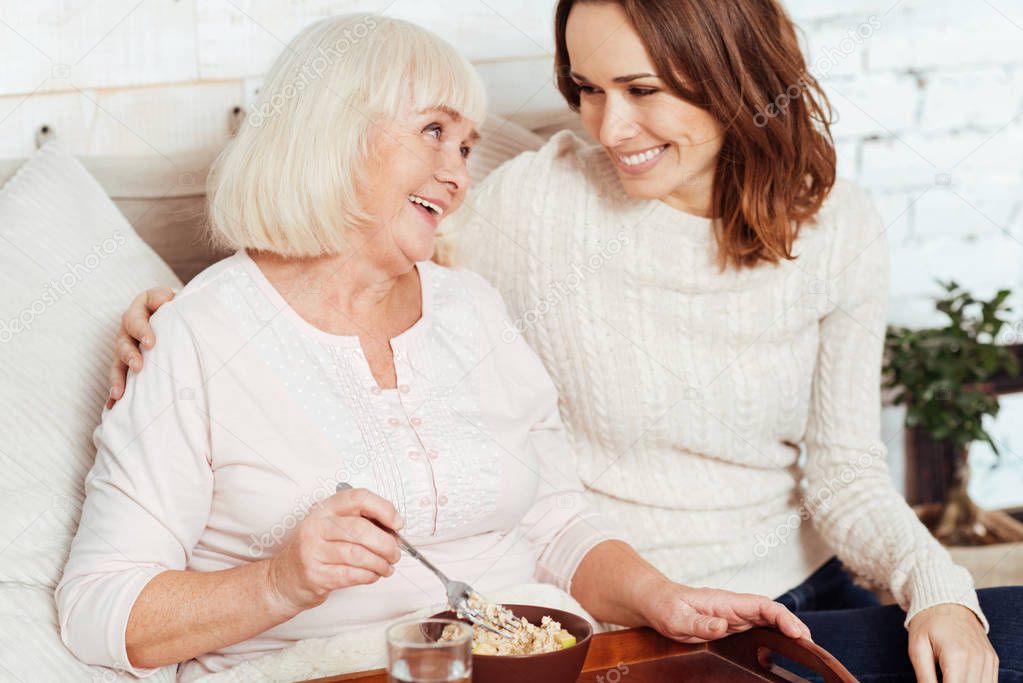 Positive sick elderly woman having breakfast in bed.