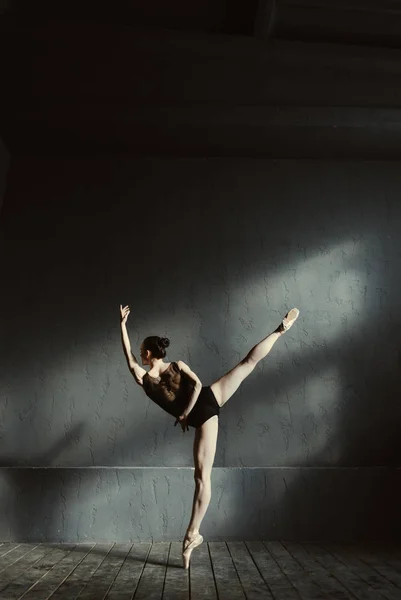 Гибкая балетная танцовщица, растянувшаяся в студии с темным освещением — стоковое фото
