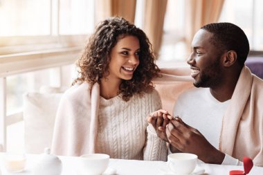 Delighted African American couple getting engaged in the cafe clipart