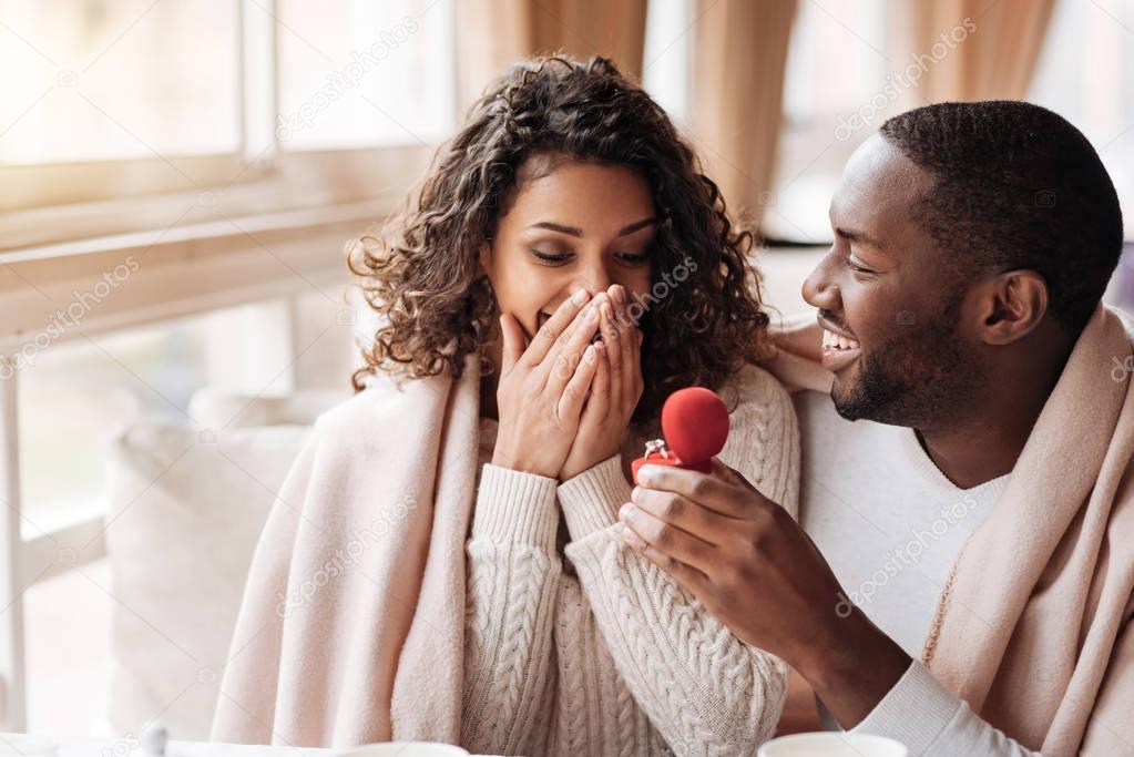 Amazed African American couple getting engaged in the cafe