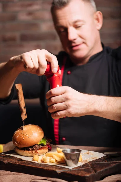 Närbild av en man som saltning pommes frites och hamburgare — Stockfoto