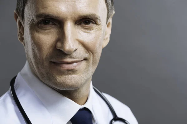 Portrét pohledný doktor s úsměvem na šedém pozadí — Stock fotografie