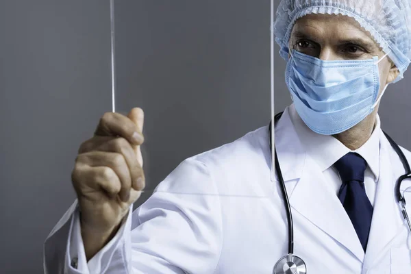 Schöner Arzt mit Gesichtsmaske, der durch medizinisches Glas schaut — Stockfoto